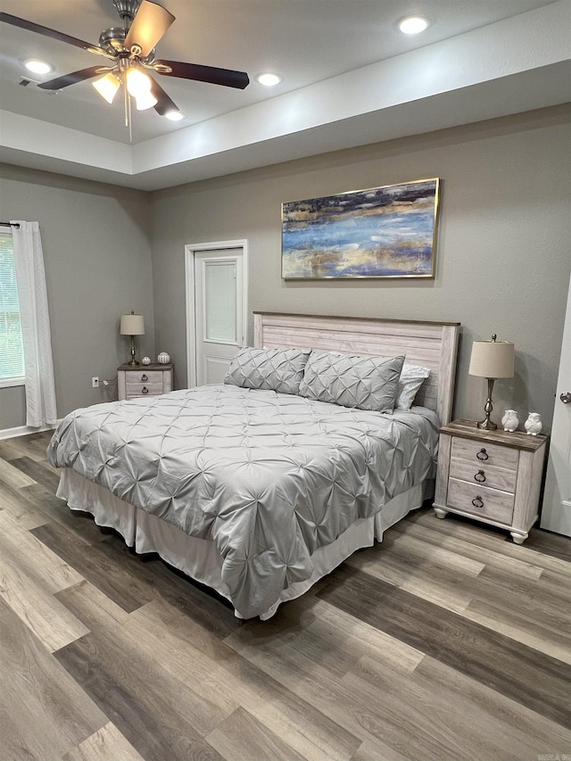 bedroom featuring recessed lighting, a ceiling fan, a tray ceiling, and wood finished floors