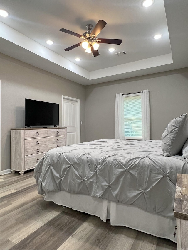 bedroom featuring a tray ceiling, recessed lighting, wood finished floors, and visible vents