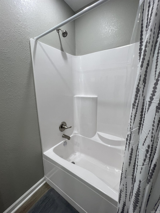 full bathroom featuring wood finished floors, shower / bath combo, a textured wall, and baseboards