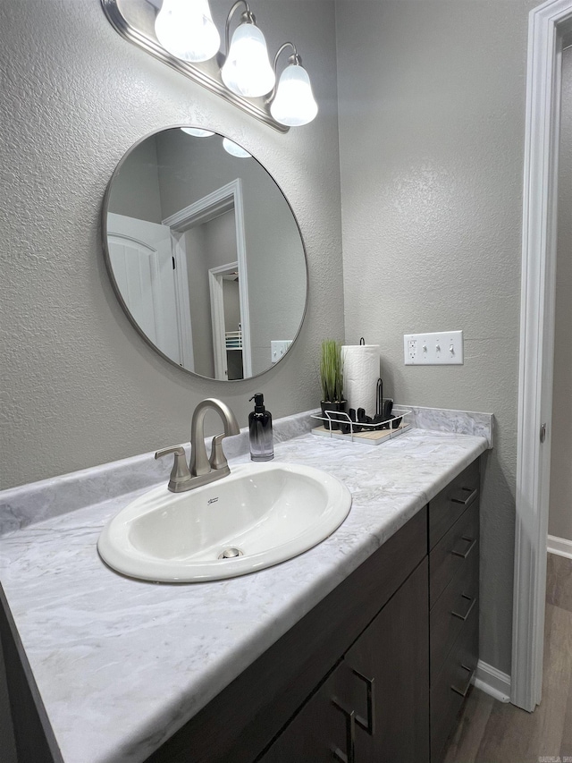 bathroom with vanity, wood finished floors, baseboards, and a textured wall