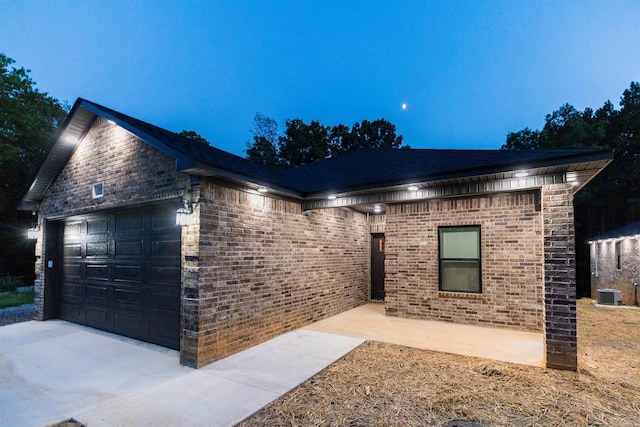 view of front facade featuring concrete driveway, central air condition unit, a garage, and brick siding