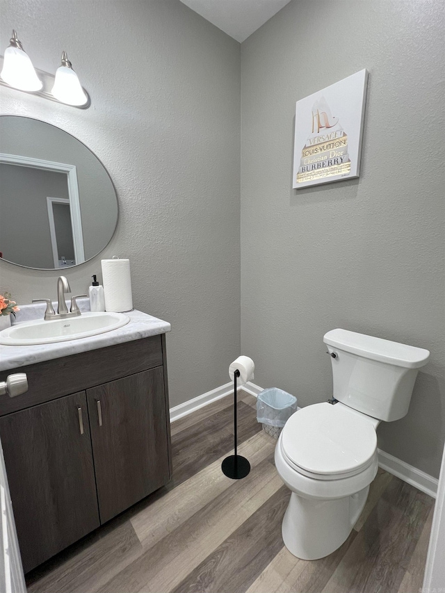 bathroom with baseboards, toilet, wood finished floors, and vanity