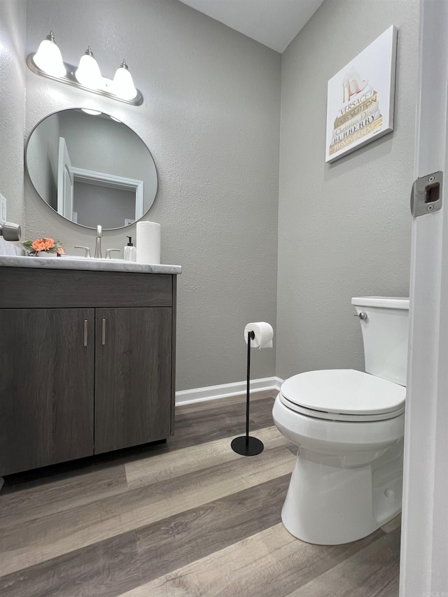 half bathroom with vanity, toilet, wood finished floors, and baseboards