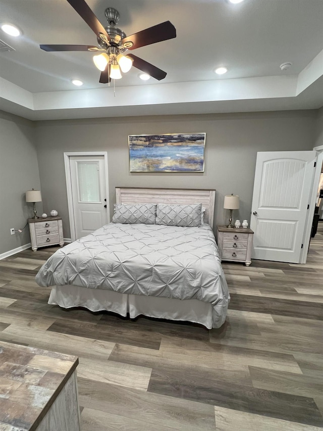 bedroom featuring recessed lighting, baseboards, a tray ceiling, and wood finished floors