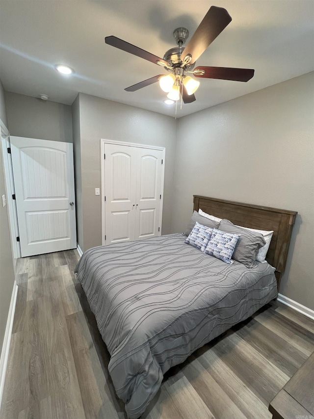 bedroom with a ceiling fan, wood finished floors, baseboards, and a closet