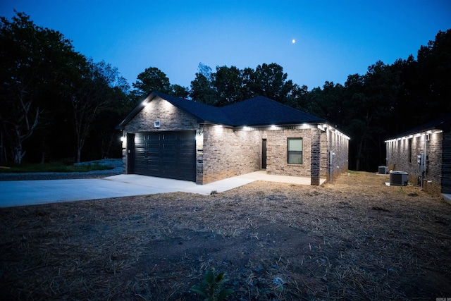 view of side of property featuring an attached garage, central AC unit, brick siding, and driveway