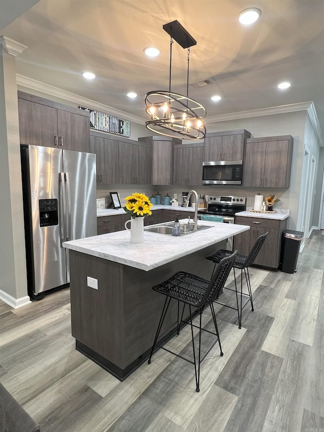 kitchen featuring a sink, stainless steel appliances, dark brown cabinetry, a breakfast bar area, and crown molding