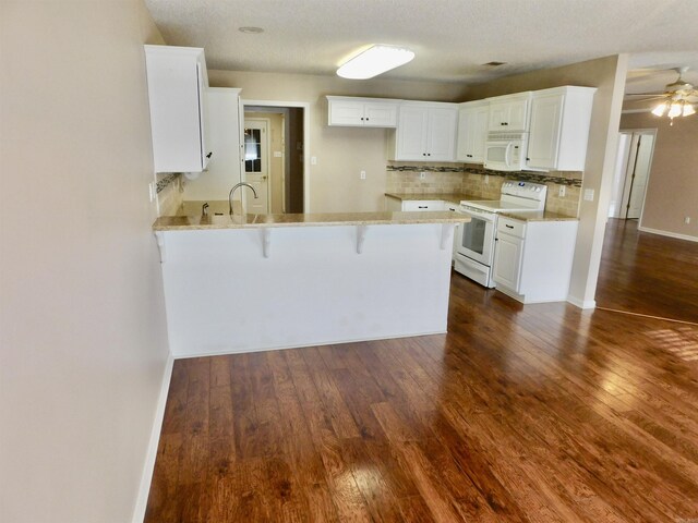 kitchen featuring decorative backsplash, a kitchen breakfast bar, a peninsula, dark wood-style floors, and white appliances