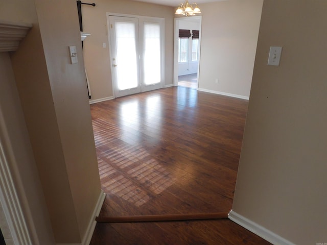 spare room featuring baseboards, an inviting chandelier, and wood finished floors