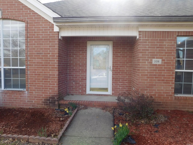 entrance to property featuring brick siding and roof with shingles