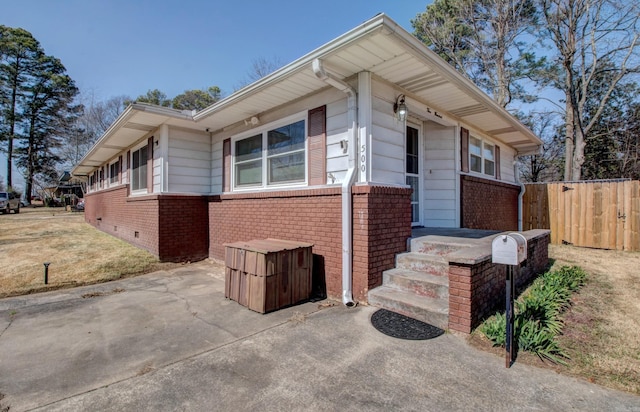 view of front facade with brick siding, crawl space, and fence