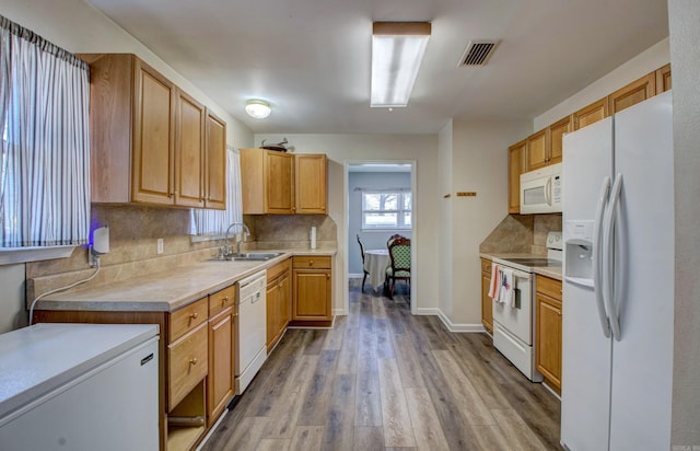 kitchen featuring light countertops, decorative backsplash, wood finished floors, white appliances, and a sink