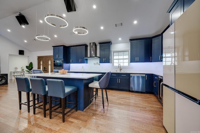 kitchen with blue cabinets, stainless steel dishwasher, wall chimney exhaust hood, and freestanding refrigerator