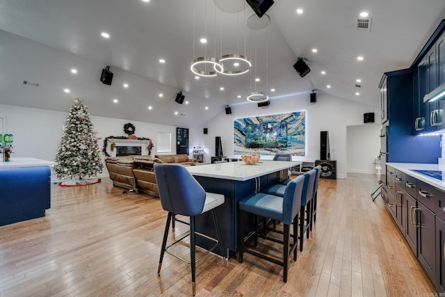 dining area featuring a glass covered fireplace, lofted ceiling, visible vents, and light wood-type flooring