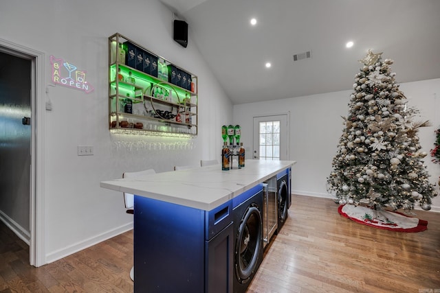 kitchen with washer and clothes dryer, visible vents, blue cabinetry, and hardwood / wood-style floors