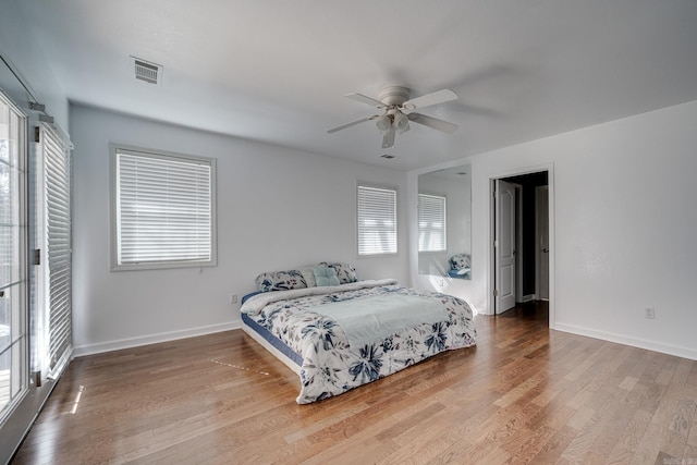 bedroom with baseboards, multiple windows, visible vents, and wood finished floors