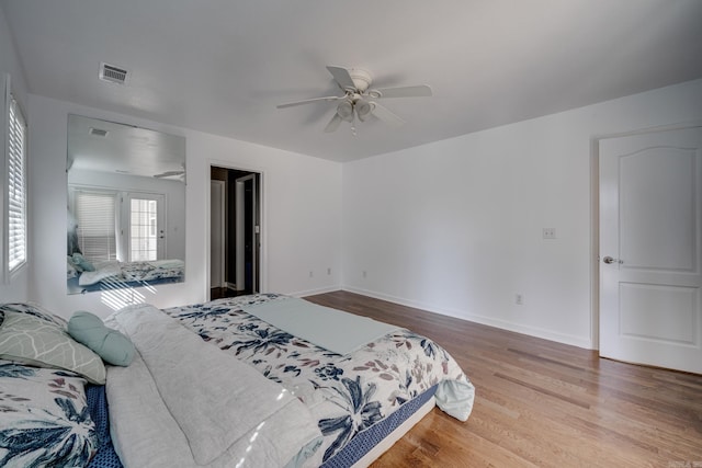 bedroom with a ceiling fan, wood finished floors, visible vents, and baseboards