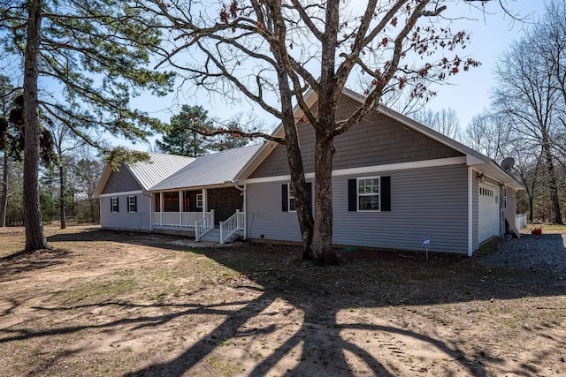 view of front of home with covered porch, an attached garage, metal roof, and dirt driveway