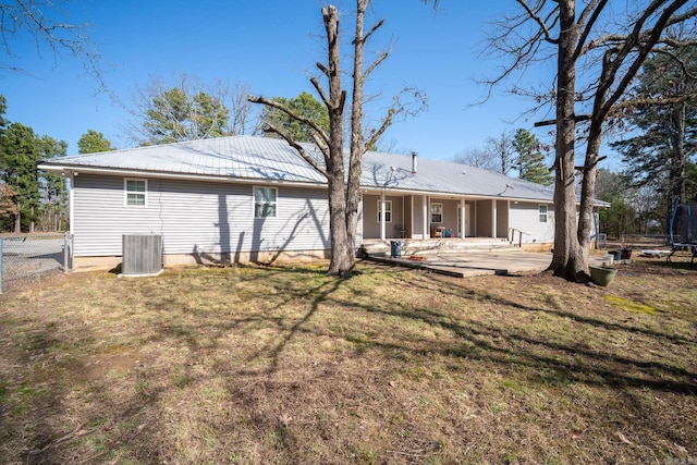 back of house featuring central AC unit, fence, a trampoline, a lawn, and metal roof