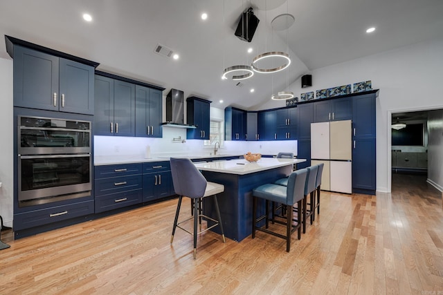 kitchen featuring blue cabinets, stainless steel double oven, wall chimney exhaust hood, and freestanding refrigerator