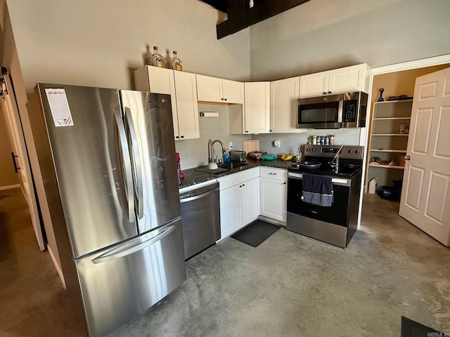 kitchen featuring a sink, dark countertops, white cabinetry, appliances with stainless steel finishes, and a towering ceiling