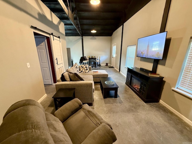 living area with a barn door, baseboards, concrete floors, and a glass covered fireplace