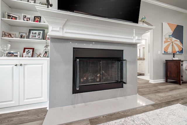 details with crown molding, a fireplace with flush hearth, wood finished floors, and baseboards