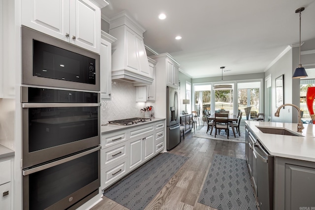 kitchen featuring crown molding, light countertops, stainless steel appliances, white cabinetry, and a sink