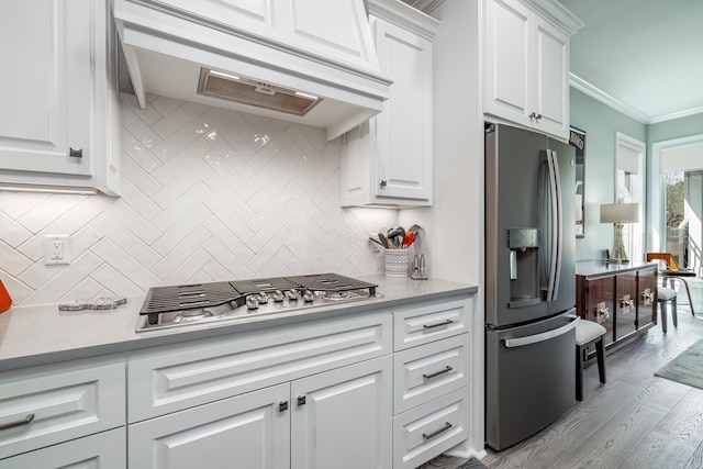 kitchen with under cabinet range hood, light countertops, ornamental molding, white cabinets, and stainless steel appliances