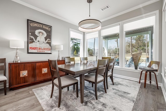 dining area with crown molding, light wood-style flooring, visible vents, and a wealth of natural light