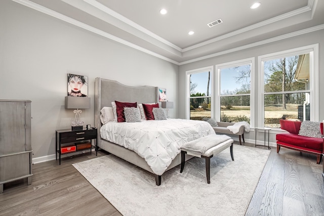 bedroom featuring a tray ceiling, baseboards, light wood-style flooring, and crown molding