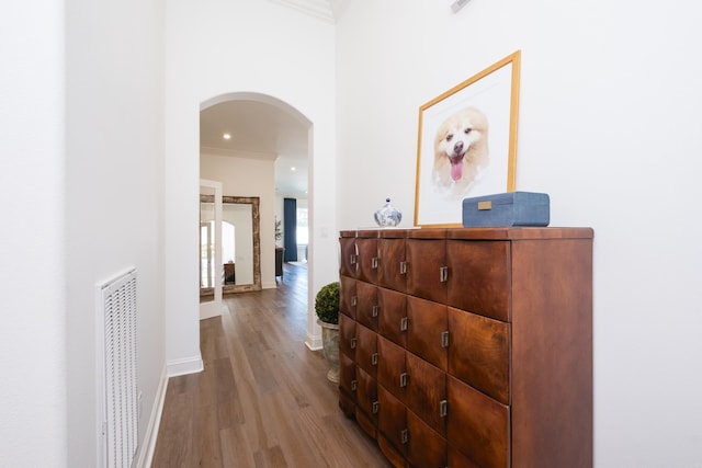 hall featuring wood finished floors, visible vents, baseboards, arched walkways, and crown molding