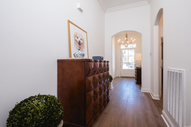 hallway featuring visible vents, dark wood-style floors, arched walkways, crown molding, and baseboards