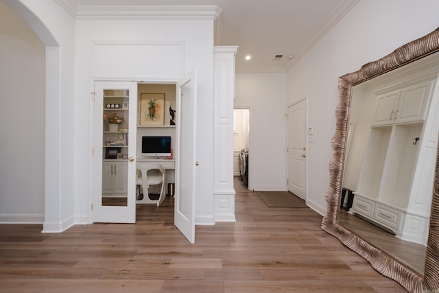 corridor with baseboards, ornamental molding, light wood-style floors, arched walkways, and washer / clothes dryer