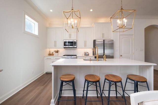 kitchen with ornamental molding, a sink, stainless steel appliances, arched walkways, and decorative backsplash