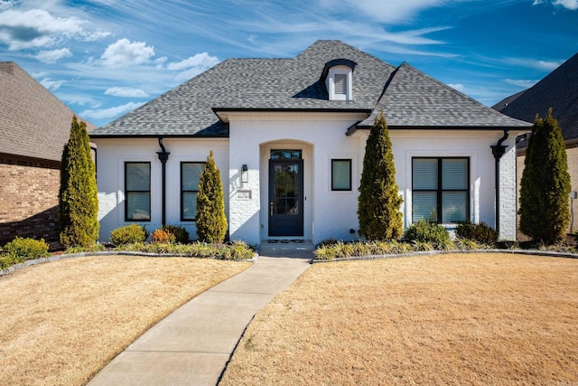 french provincial home featuring a shingled roof and a front yard