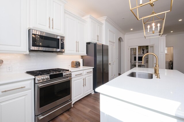 kitchen with tasteful backsplash, ornamental molding, appliances with stainless steel finishes, arched walkways, and a sink