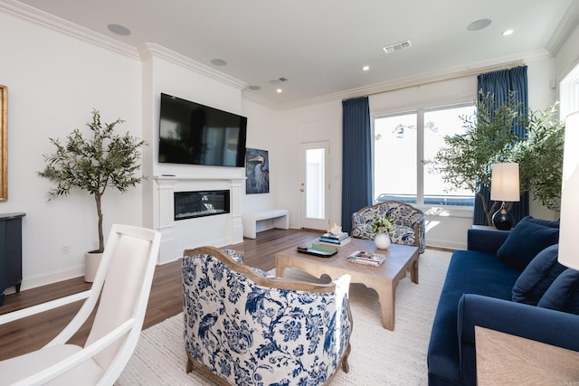 living area featuring visible vents, wood finished floors, a glass covered fireplace, and ornamental molding