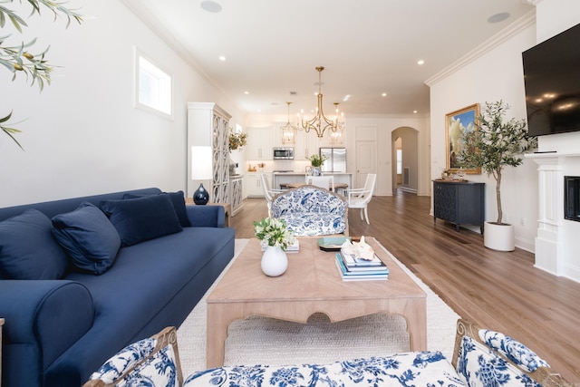 living room featuring arched walkways, a fireplace, crown molding, and light wood-style floors