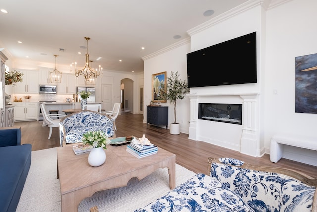 living area featuring wood finished floors, recessed lighting, arched walkways, ornamental molding, and a glass covered fireplace