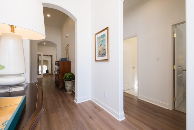 corridor with baseboards, ornamental molding, recessed lighting, wood finished floors, and arched walkways