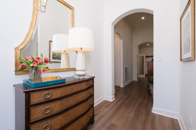 hall with visible vents, arched walkways, dark wood-type flooring, and baseboards