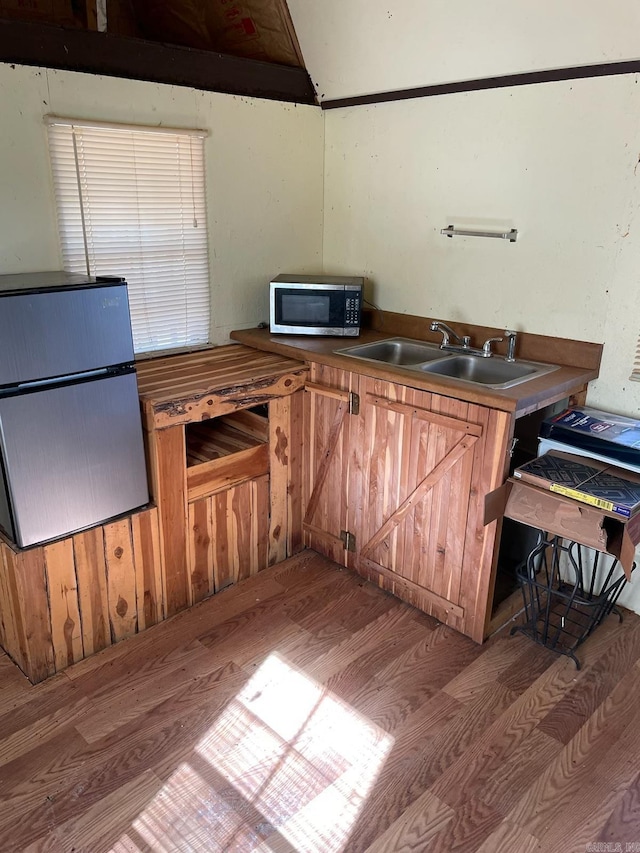 kitchen with stainless steel microwave, brown cabinets, wood finished floors, and a sink