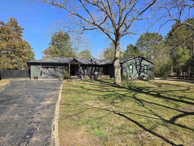 mid-century home featuring aphalt driveway, an attached garage, fence, and a front yard