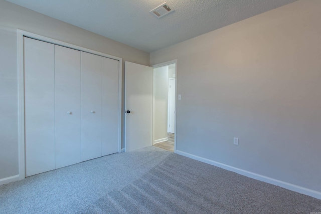 unfurnished bedroom with visible vents, a textured ceiling, a closet, carpet flooring, and baseboards