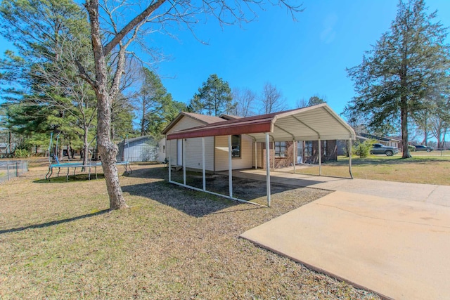 exterior space featuring a detached carport, driveway, a trampoline, and fence