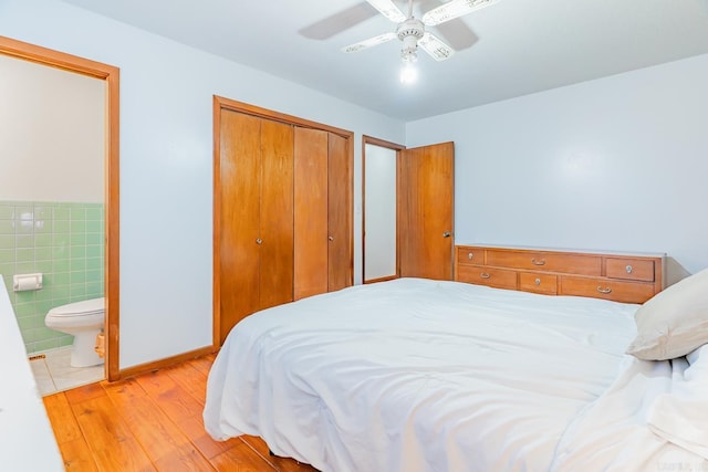 bedroom with a ceiling fan, connected bathroom, a closet, light wood-style floors, and tile walls