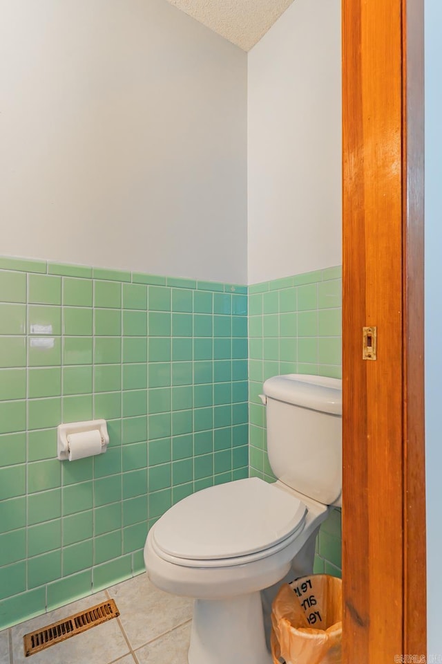 bathroom with visible vents, tile walls, toilet, tile patterned floors, and a textured ceiling