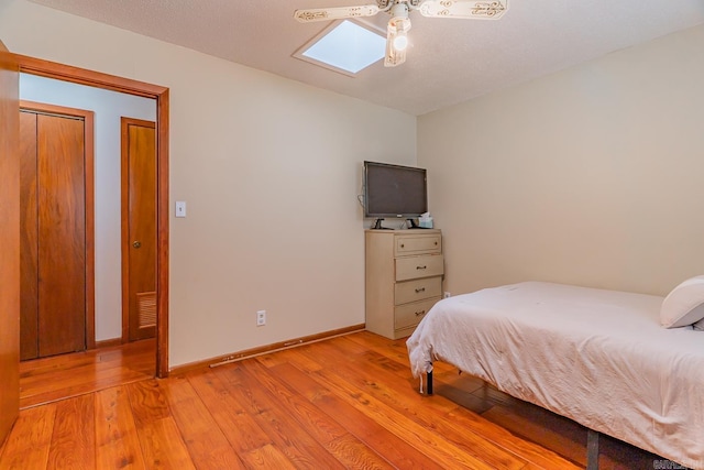 bedroom with baseboards, ceiling fan, a skylight, and light wood-style floors