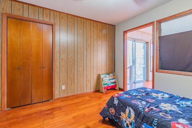 bedroom featuring baseboards, wooden walls, and light wood-style flooring